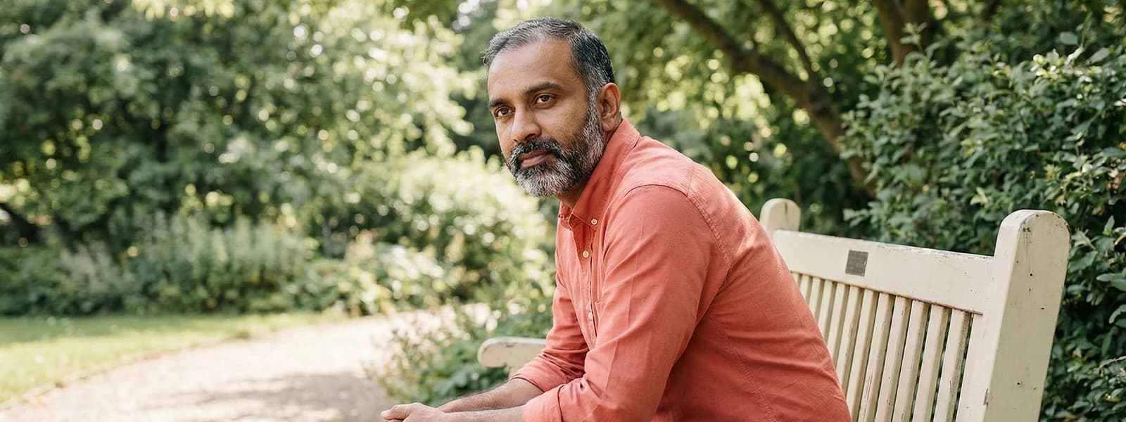Indian man sitting thoughtfully on a bench in a green park