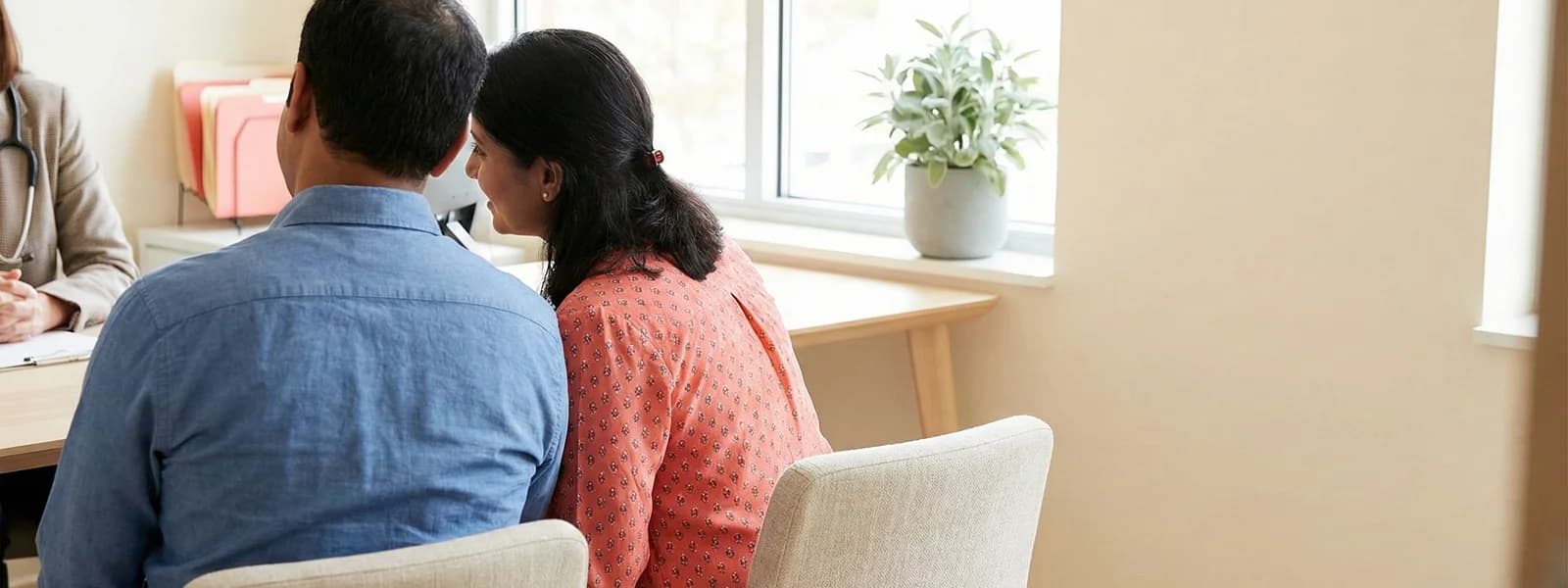 South Asian couple sitting side by side in a modern medical office, seen from behind
