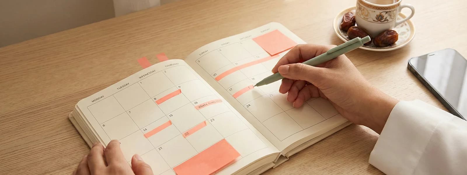 Womans hands holding pen over a planner with coloured sticky notes and Arabic coffee